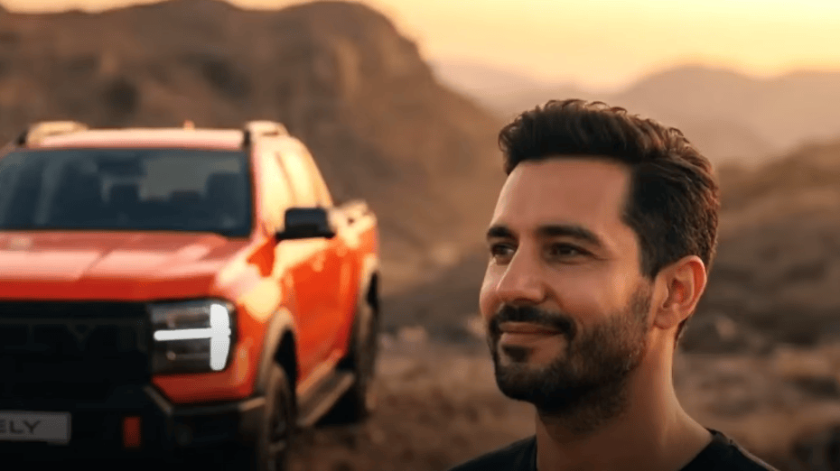 Driver standing beside an orange Rely R8 at sunset